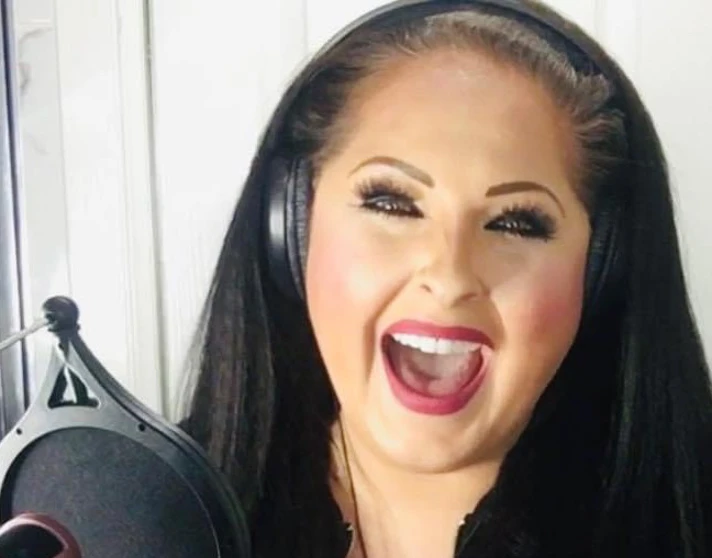 Lisa Jayne Rattray sings into a microphone in a recording studio, smiling brightly and wearing headphones and a sparkly black outfit. Lisa Jayne Rattray sings into a microphone in a recording studio, smiling brightly and wearing headphones and a sparkly black outfit.